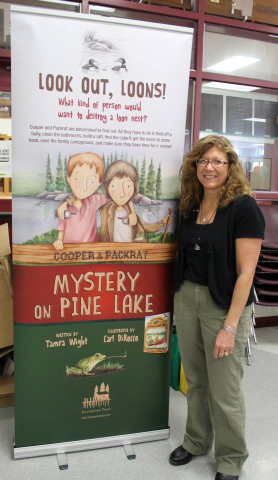Tamra standing next to a banner for Mystery On Pine Lake